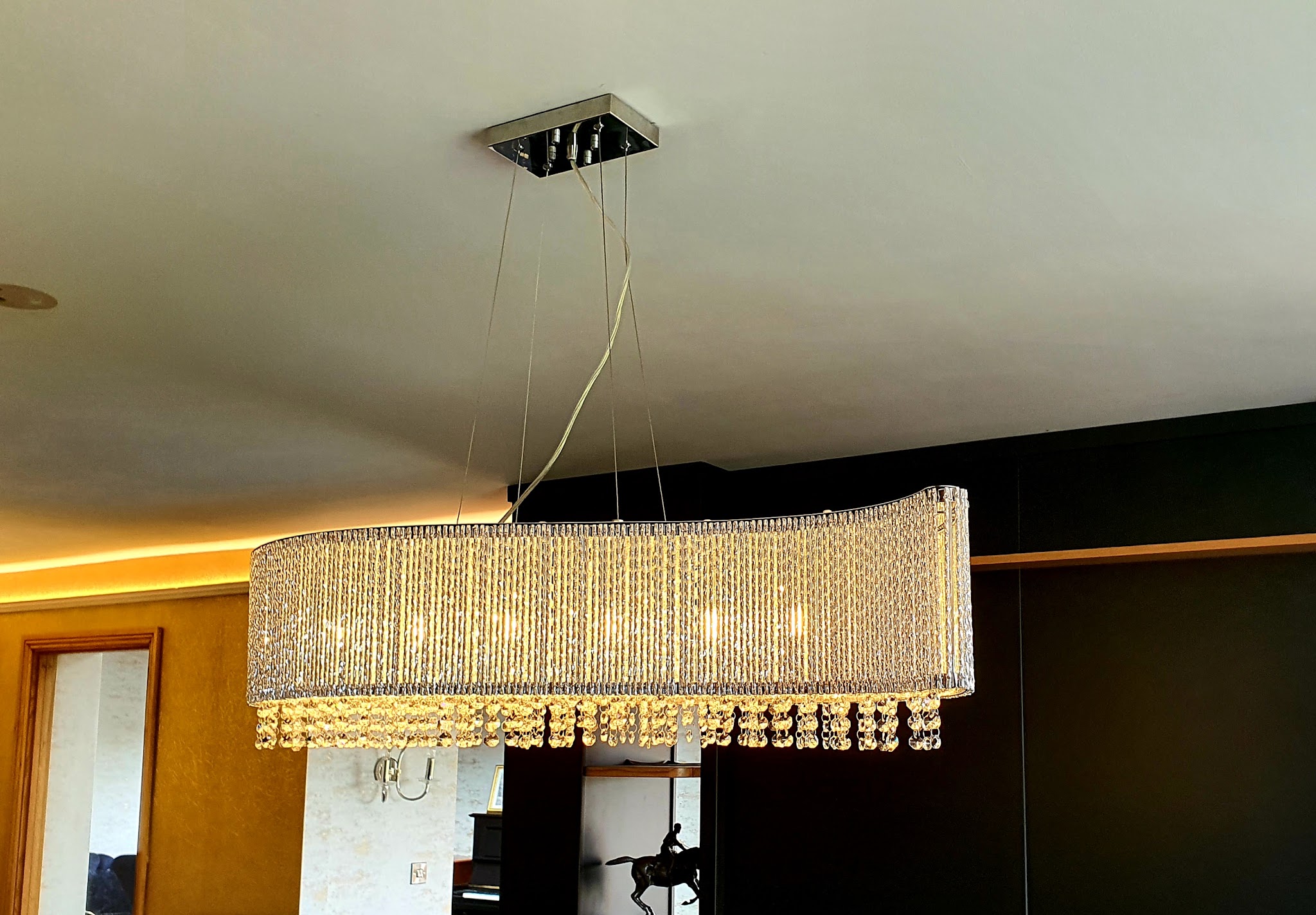 A long crystal pendant over a dining area with warm strip lighting